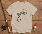 Beige t-shirt with 'Addicted' and fish hook design on a wooden surface with fishing equipment.

