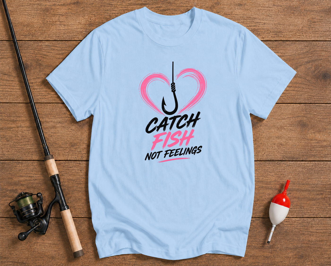 Light blue t-shirt with fishing-themed graphic on a wooden surface with fishing equipment.