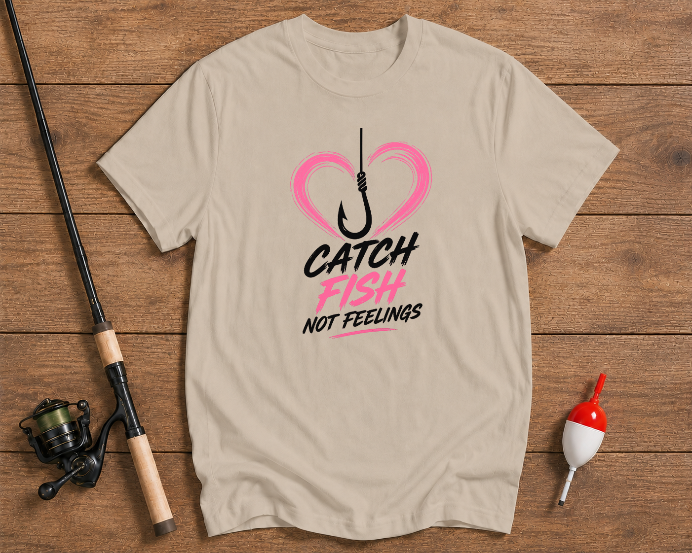 Beige t-shirt with fishing graphic and text on a wooden surface with fishing equipment.

