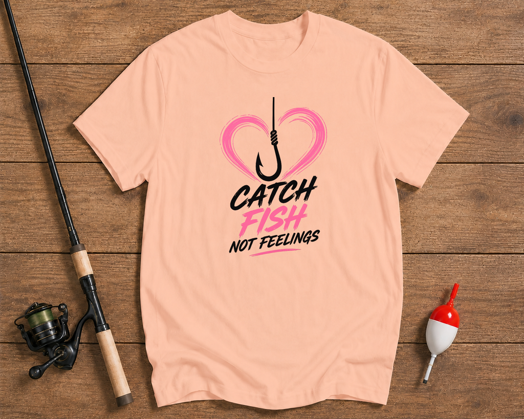 Pink t-shirt with fishing graphic and text on a wooden surface with fishing equipment.


