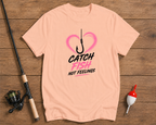 Pink t-shirt with fishing graphic and text on a wooden surface with fishing equipment.


