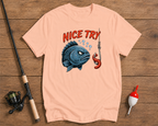 Pink t-shirt with a graphic of a fish and lobster on a wooden surface with fishing equipment.

