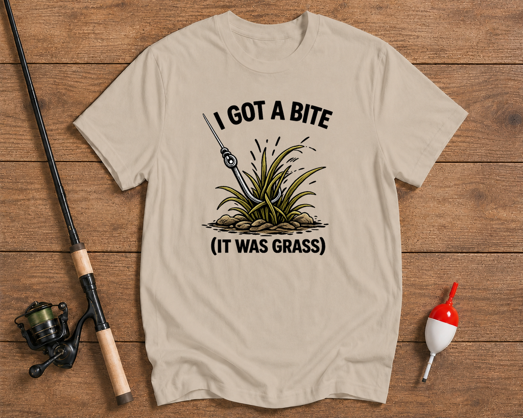 Beige t-shirt with fishing graphic and text on a wooden surface with fishing equipment.

