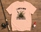 Pink t-shirt with fishing graphic and text on a wooden surface with fishing equipment.

