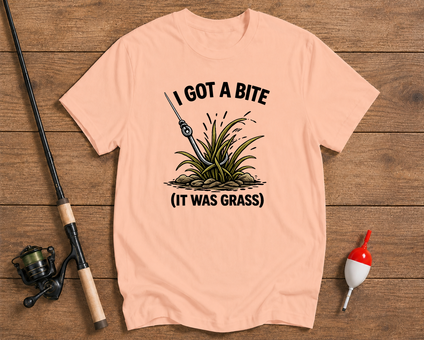Pink t-shirt with fishing graphic and text on a wooden surface with fishing equipment.

