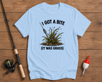 Light blue t-shirt with fishing graphic and text on a wooden surface with fishing equipment.

