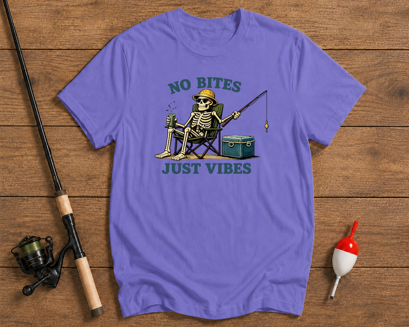 Purple t-shirt with skeleton fishing graphic and 'No Bites Just Vibes' text on a wooden surface with fishing equipment.

