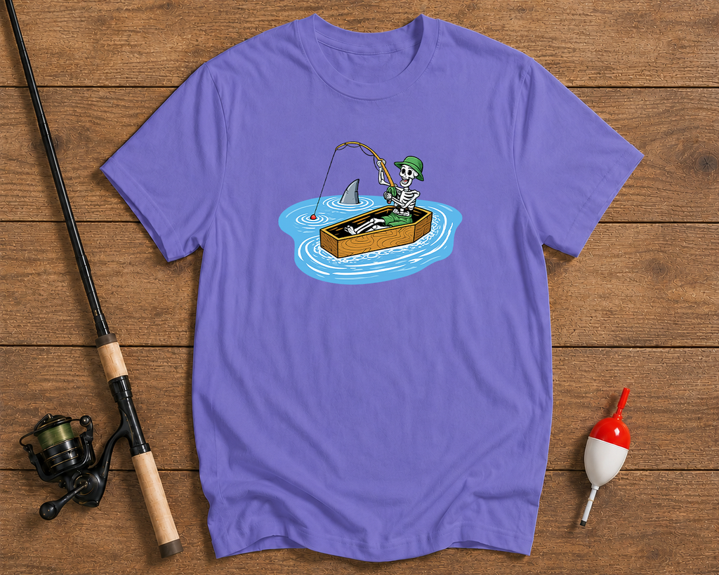 Purple t-shirt with a graphic of a skeleton fishing, placed on a wooden surface with fishing equipment.

