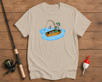 Beige t-shirt with a cartoon design of a skeleton fishing, placed on a wooden surface with fishing equipment.


