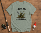 Light green t-shirt with fishing graphic and text on a wooden surface with fishing equipment.

