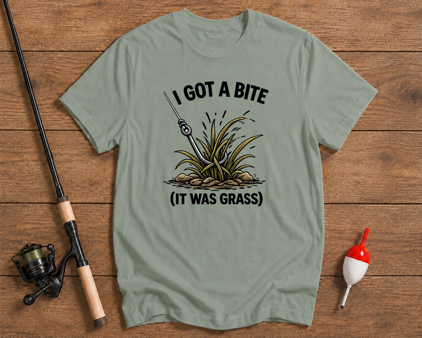 Light green t-shirt with fishing graphic and text on a wooden surface with fishing equipment.

