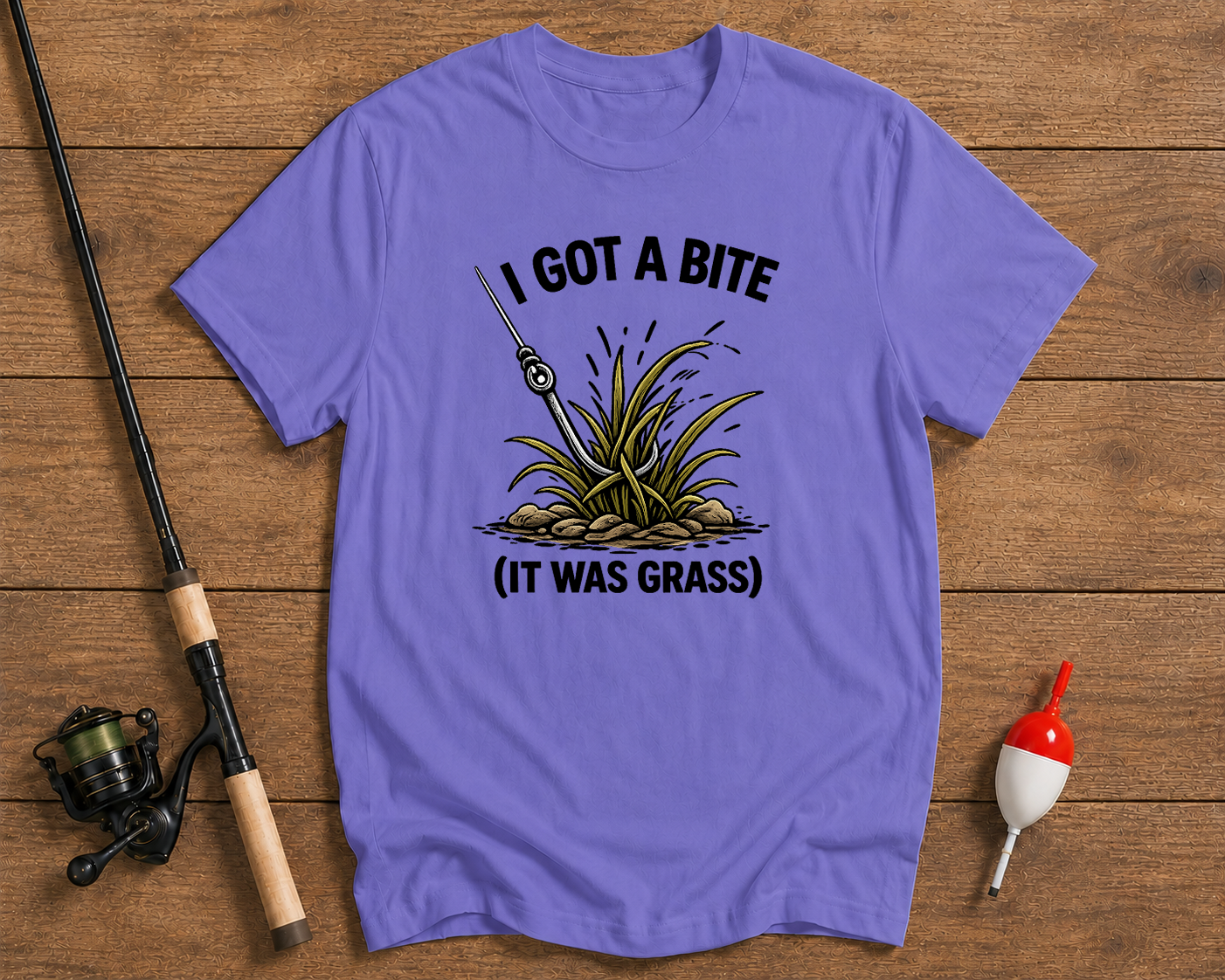 Purple t-shirt with fishing graphic and text on a wooden surface with fishing equipment.

