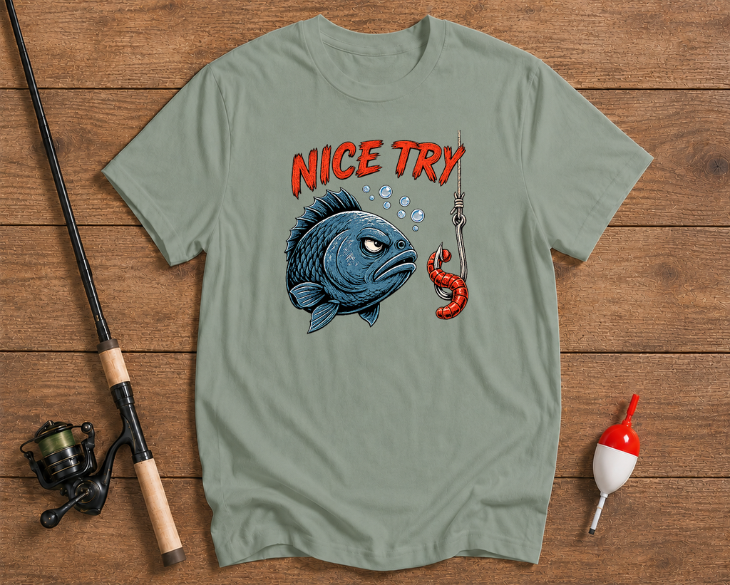 Green t-shirt with fish graphic and 'Nice Try' text on a wooden surface with fishing equipment.

