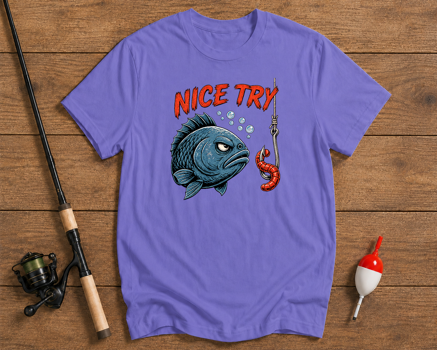 Purple t-shirt with a fish graphic and 'Nice Try' text on a wooden surface with fishing equipment.

