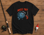Black t-shirt with a fish graphic and 'Nice Try' text on a wooden surface with fishing equipment.


