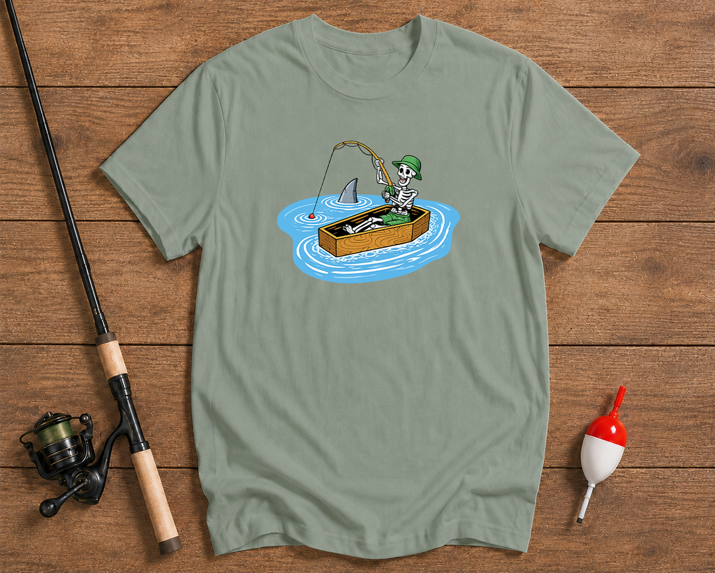 Green t-shirt with a skeleton fishing design on a wooden surface with fishing equipment.

