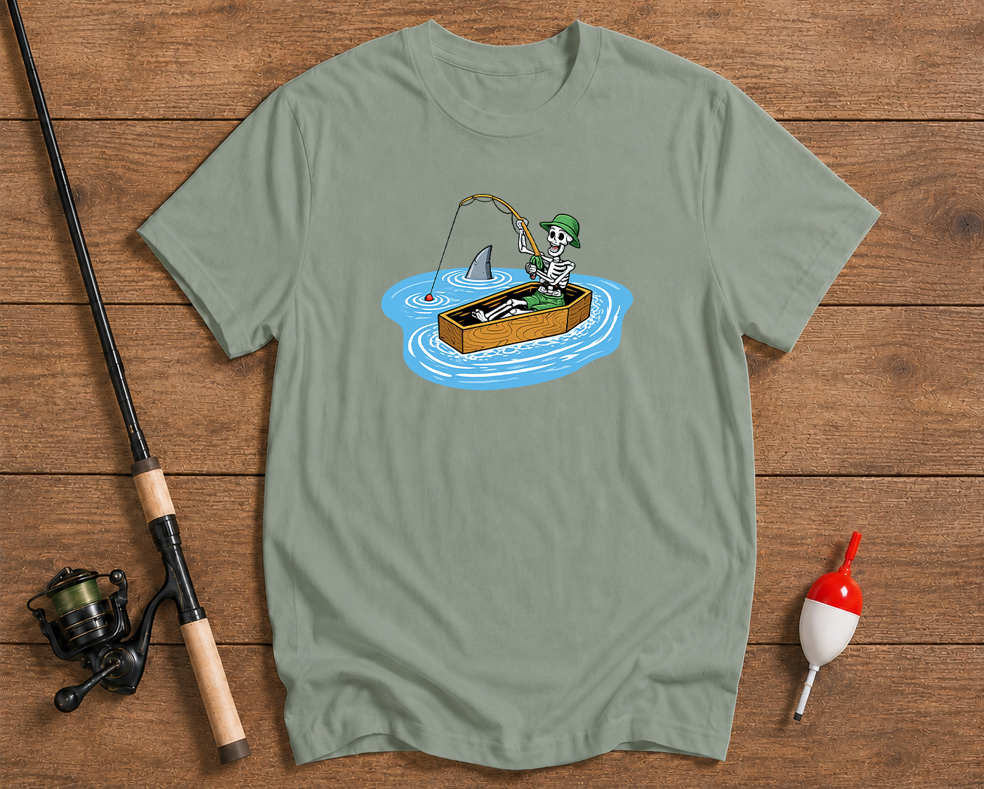 Green t-shirt with a skeleton fishing design on a wooden surface with fishing equipment.

