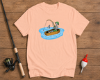 Pink t-shirt with a graphic of a skeleton fishing, placed on a wooden surface with fishing equipment.

