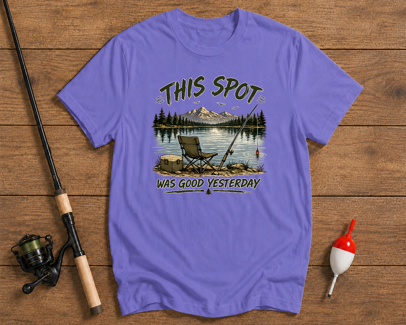 Purple t-shirt with fishing graphic and text on a wooden surface with fishing equipment.

