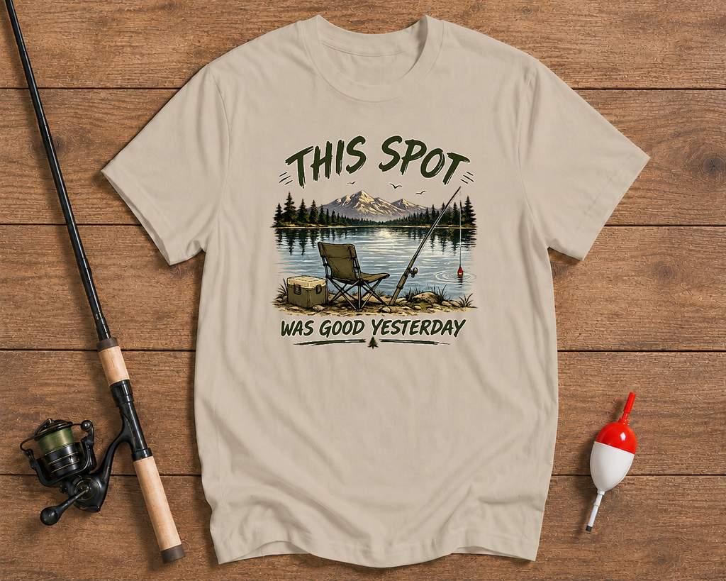Beige t-shirt with nature graphic and text on a wooden surface with fishing equipment.

